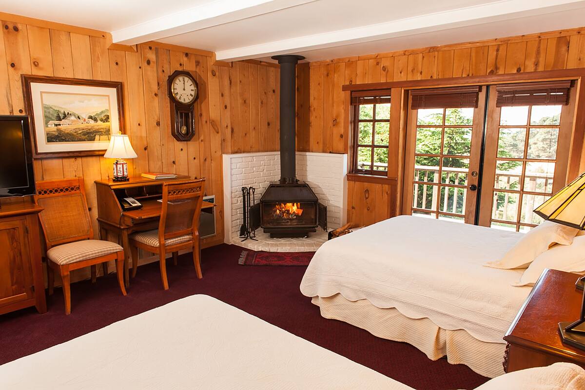 A room with a fireplace, wooden walls, a bed, a desk with a chair, and a television.
