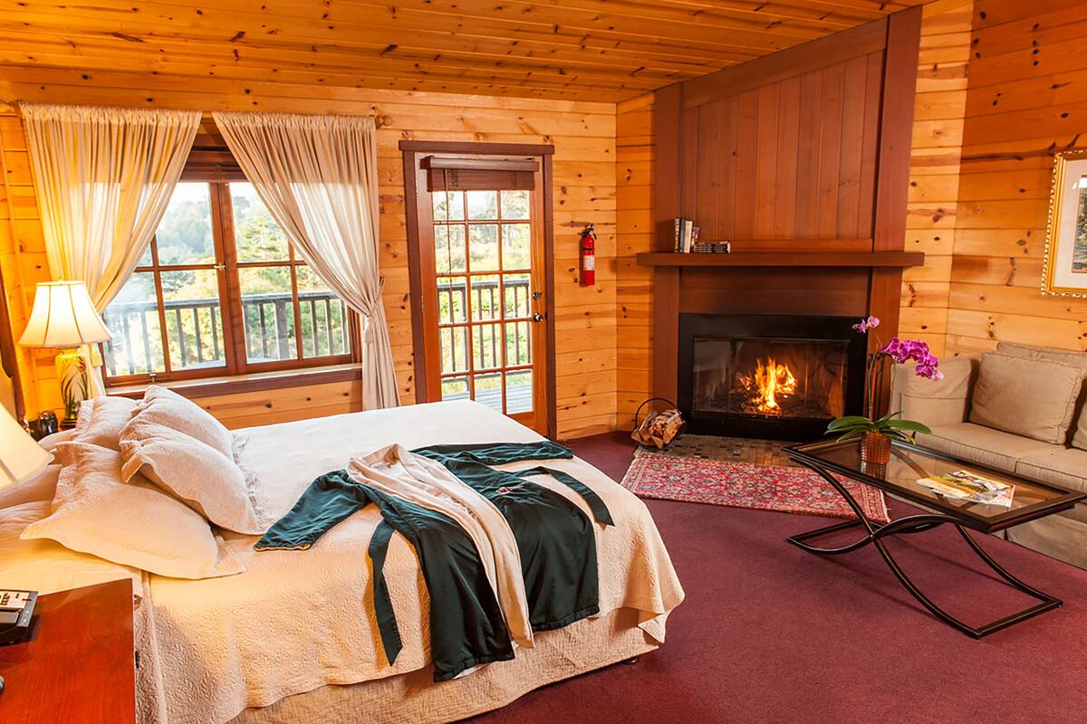 A cozy log cabin room with a bed, a sofa, a fireplace, and a window with curtains.