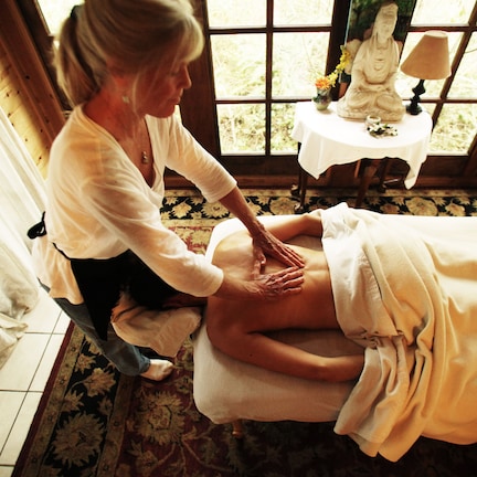 A massage therapy session in a room with a large window, a statue, and a small table with a lamp.