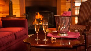 Un cuarto acogedor con chimenea, un sofá rojo, dos copas de champán y un balde con una botella y un corcho.