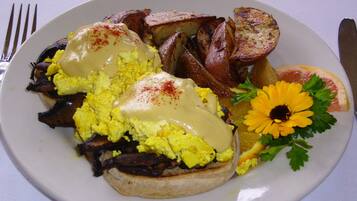 A plate of eggs benedict with hollandaise sauce, roasted potatoes, and a garnish of parsley and a yellow flower.