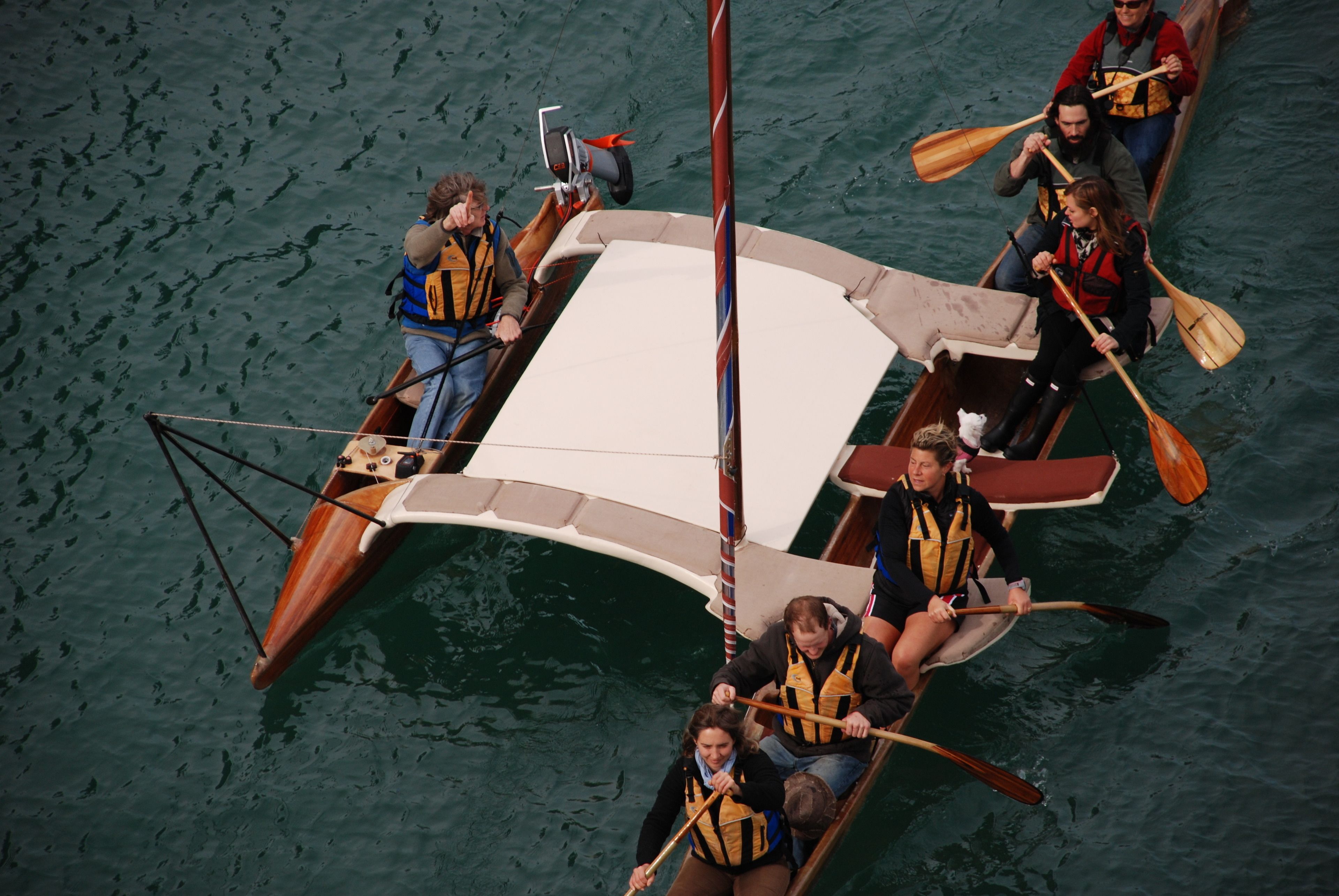 A group of people in a wooden boat with a white canopy, paddling on a body of water.