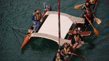 A group of people in a wooden boat with a white canopy, paddling on a body of water.