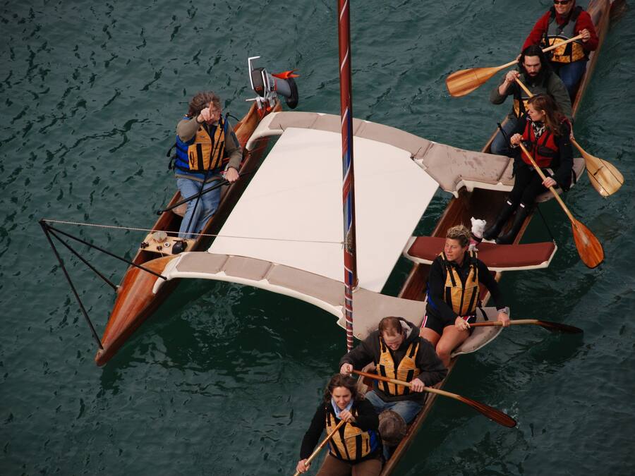 A group of people in a wooden boat with a white canopy, paddling on a body of water.