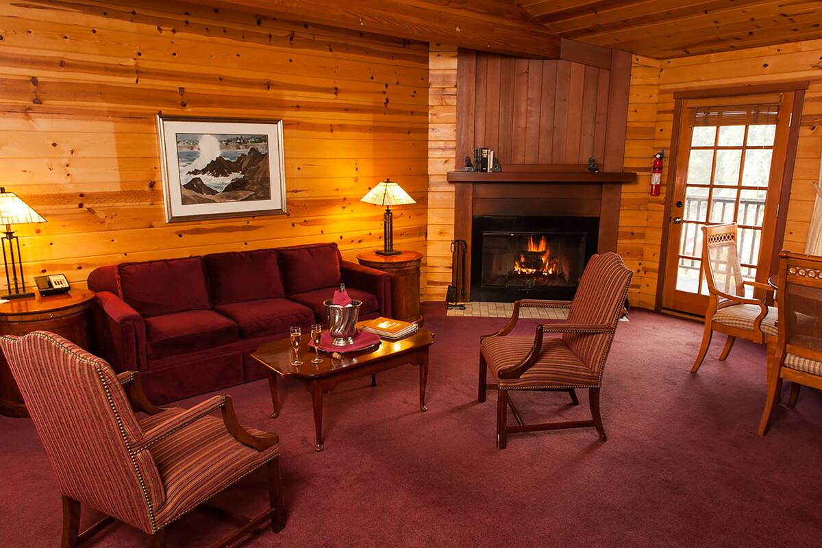 A cozy log cabin interior with a fireplace, a red sofa, striped chairs, and a framed picture on the wall.