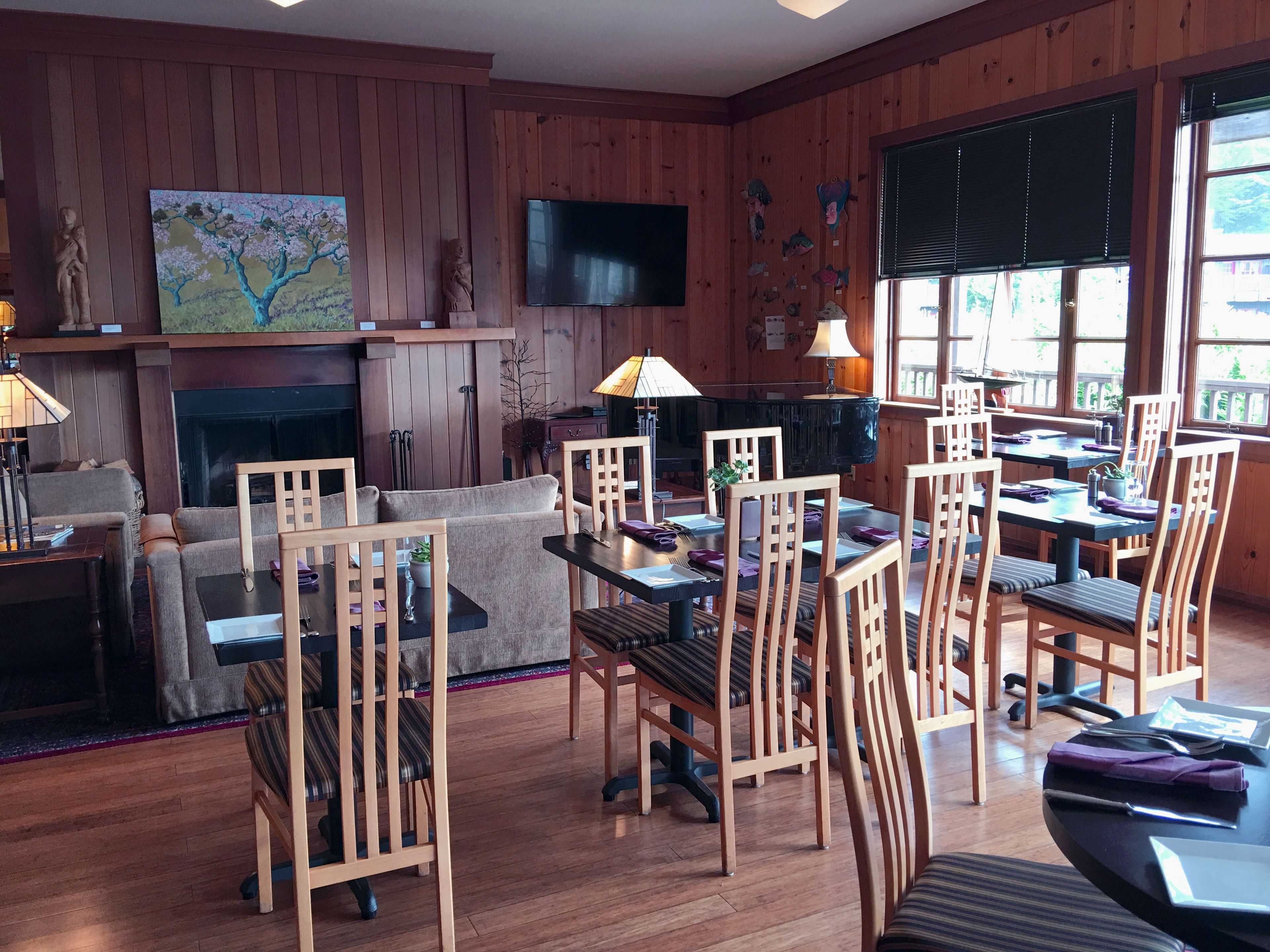 A cozy living room with a fireplace, wooden walls, a flat-screen TV, and a dining area with wooden chairs and tables.