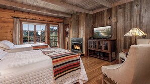 A cozy cabin-style room with two beds, a fireplace, a television, and a lamp.