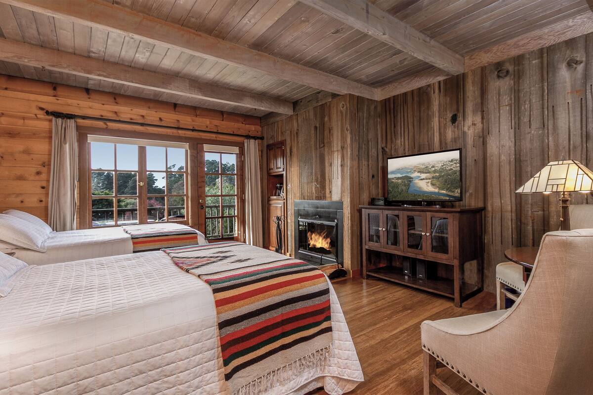 A cozy cabin-style room with two beds, a fireplace, a television, and a lamp.