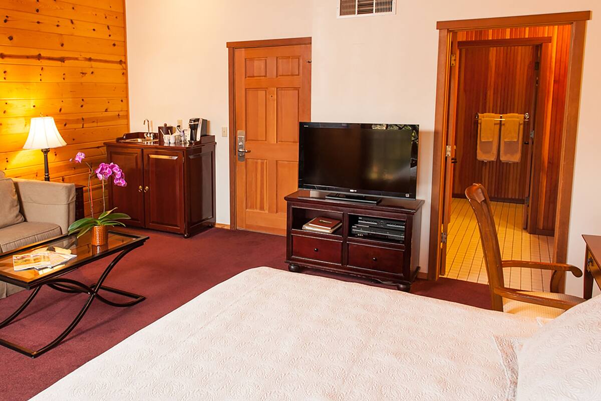 A living room with a sofa, a coffee table, a TV stand with a flat-screen TV, a wooden door, and a framed picture on the wall.