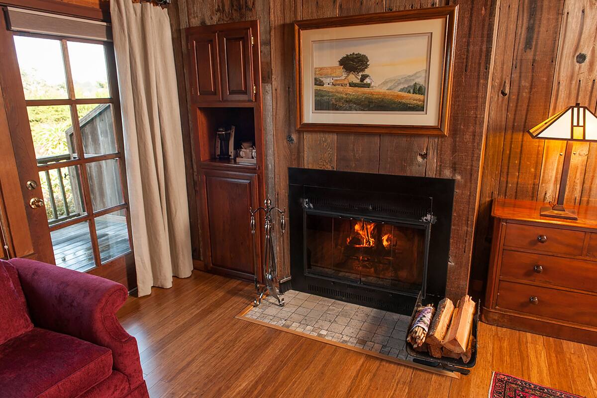 A cozy room with a fireplace, wooden walls, a red sofa, and a framed landscape painting.