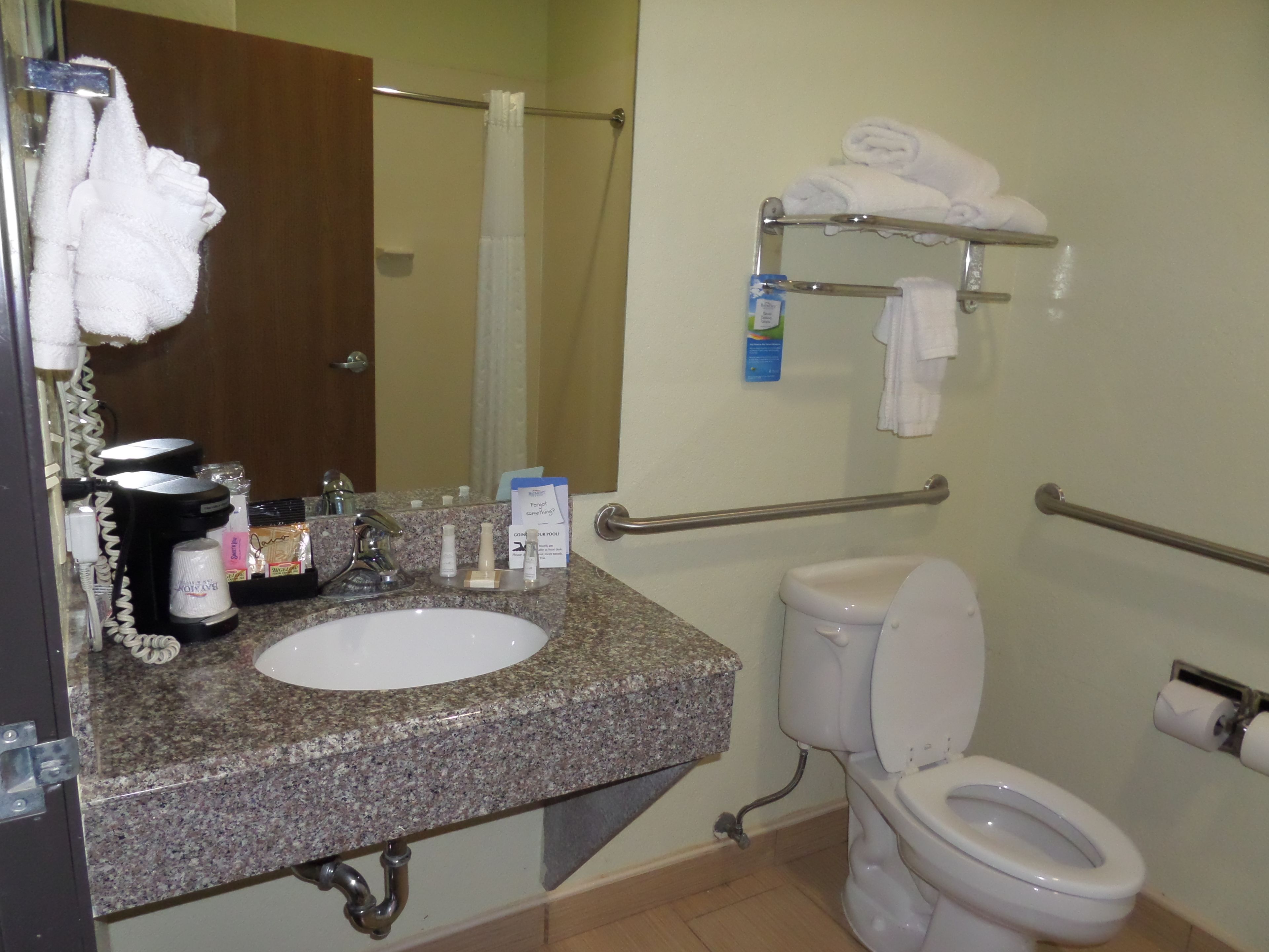 A bathroom with a granite sink, toilet, and handrails.
