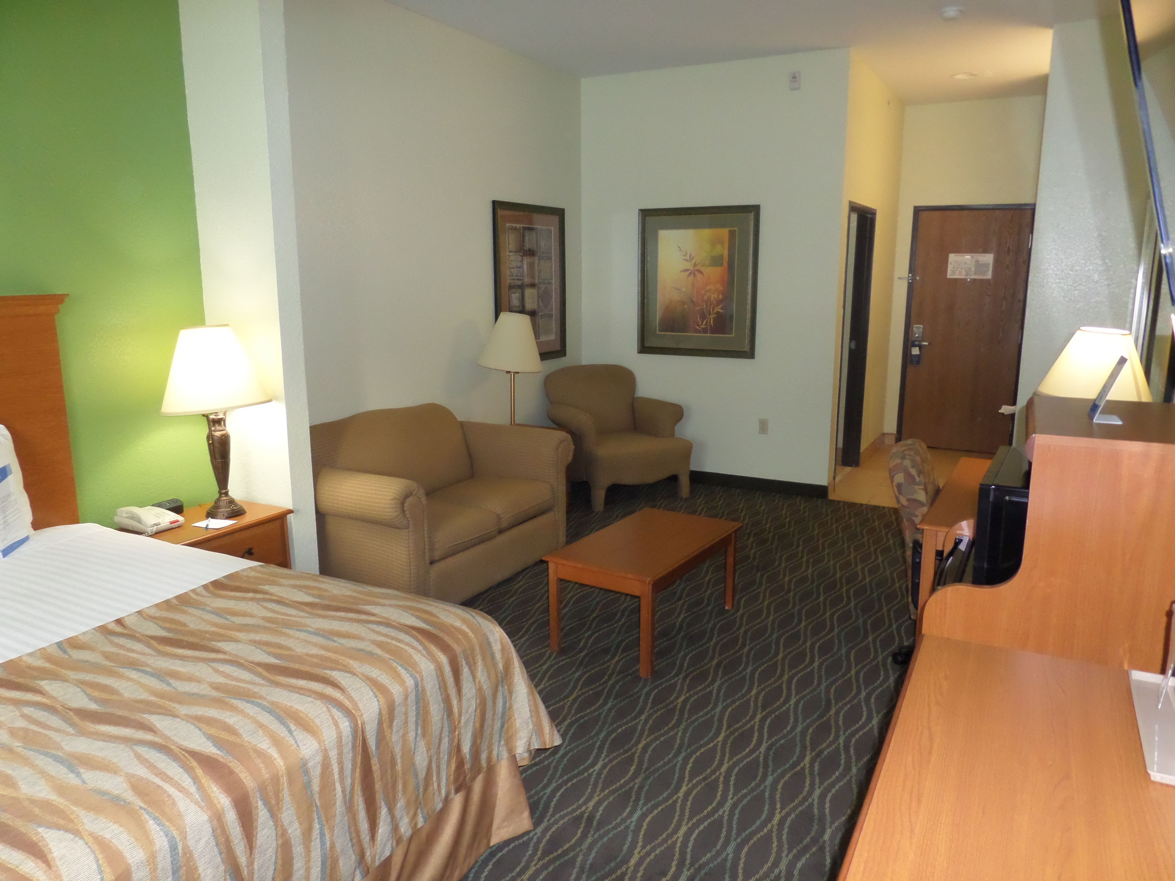 A hotel room with a bed, two armchairs, a small table, a desk, a lamp, and two framed pictures on the wall.