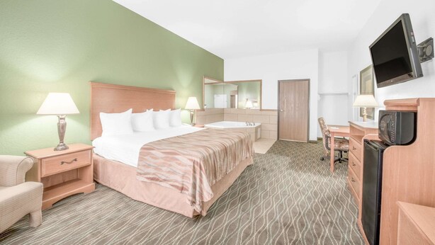 A hotel room with a bed, a desk, a chair, a television, and a bathroom. - Baymont by Wyndham Pearsall (Pearsall)