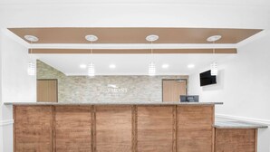 A reception area with a wooden counter, a stone backsplash, and a flat-screen TV mounted on the wall. - Baymont by Wyndham Pearsall (Pearsall)