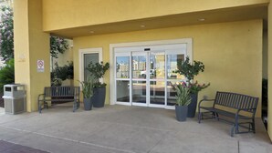 A building entrance with a yellow facade, a no smoking sign, and two benches outside. - Baymont by Wyndham Pearsall (Pearsall)