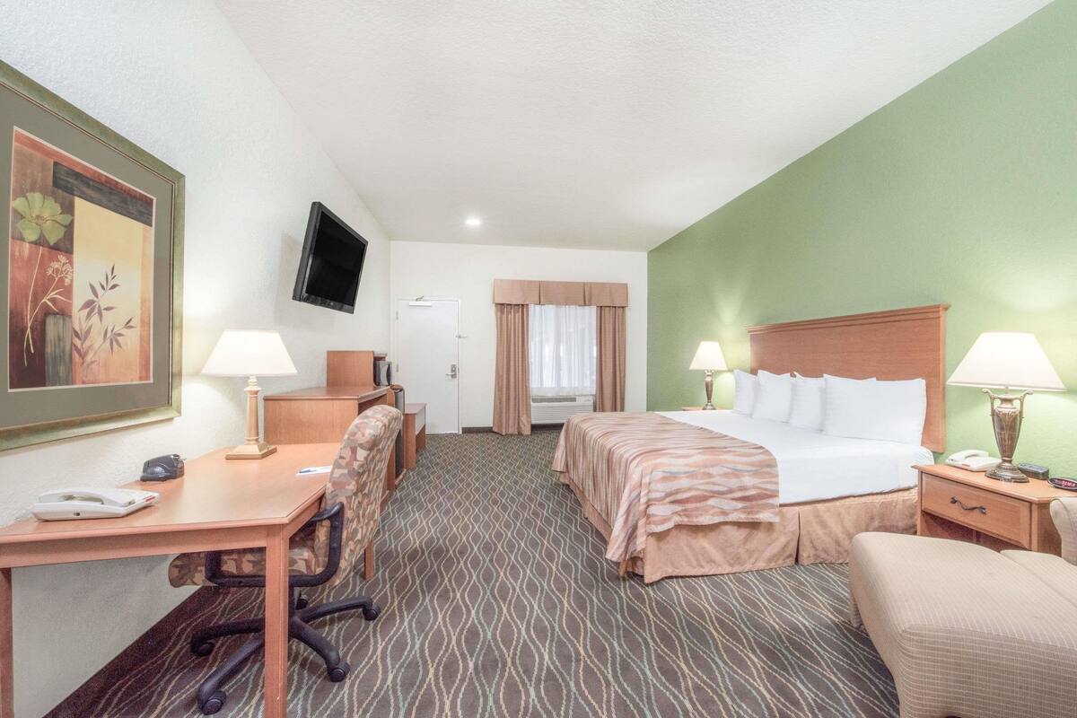 A hotel room with a bed, desk, chair, and a television on the wall.