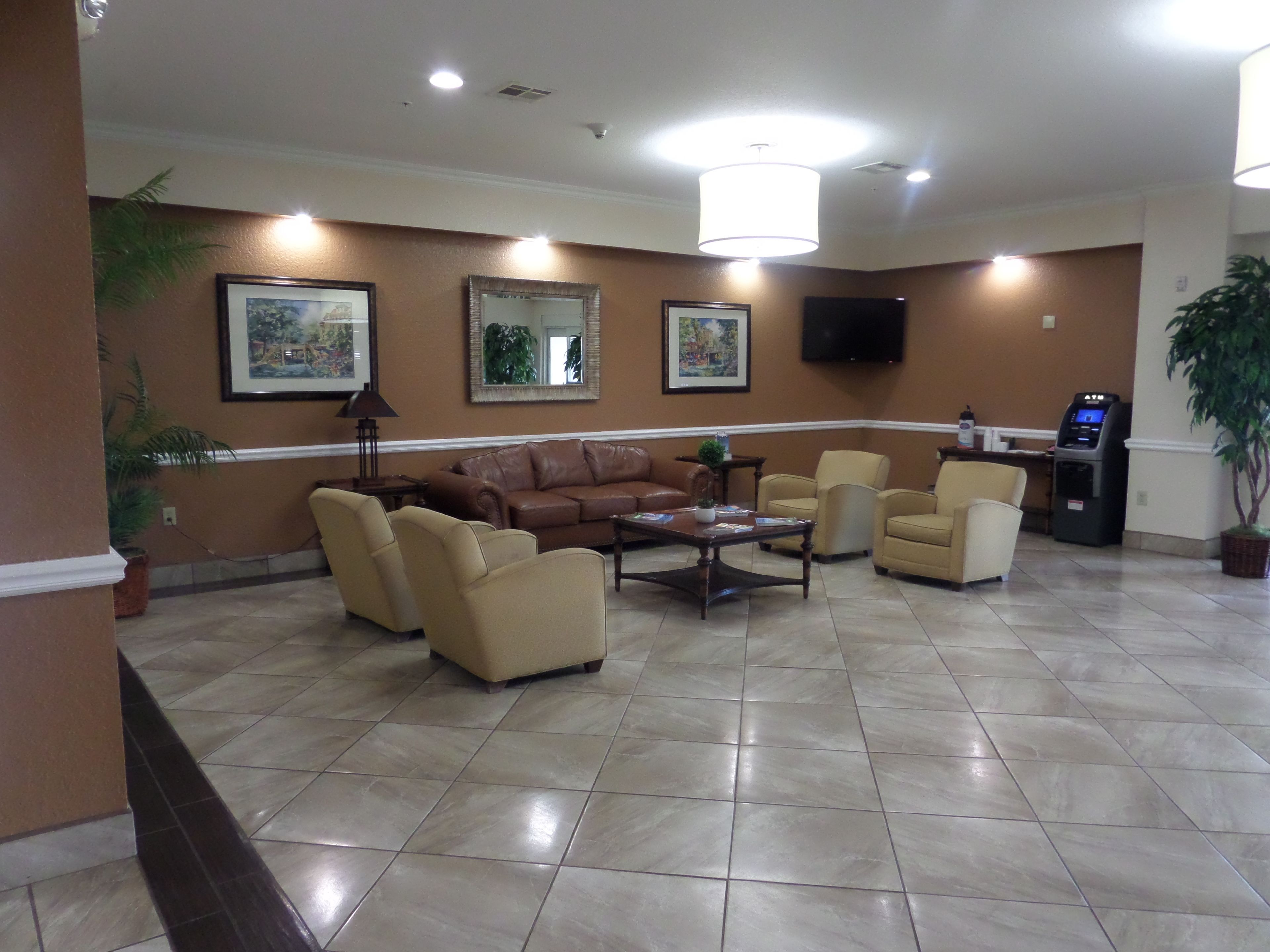 Un hall con un sofá de cuero marrón, sillones beige, una mesa de centro y un televisor montado en la pared.