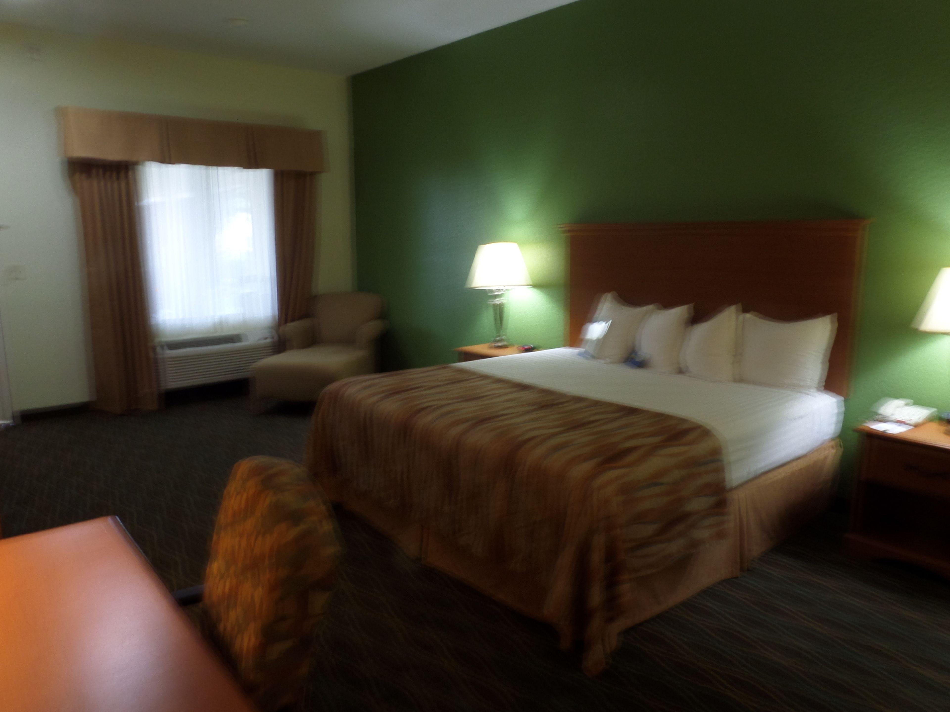 Una habitación de hotel con una cama grande, una silla, un escritorio y una mesita de noche con lámpara.