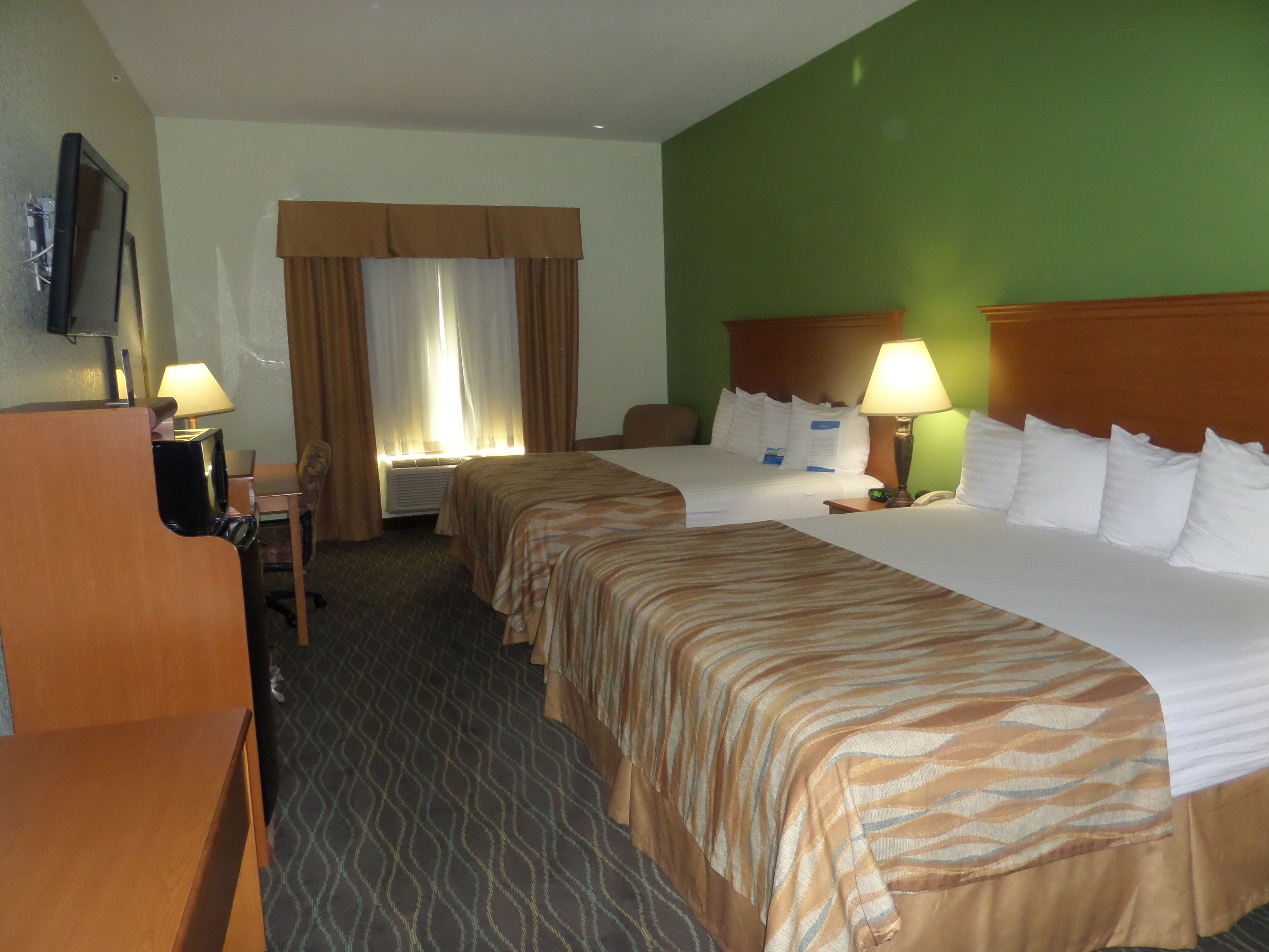 Habitación de hotel con dos camas, un escritorio, una silla, un televisor y una ventana con cortinas.