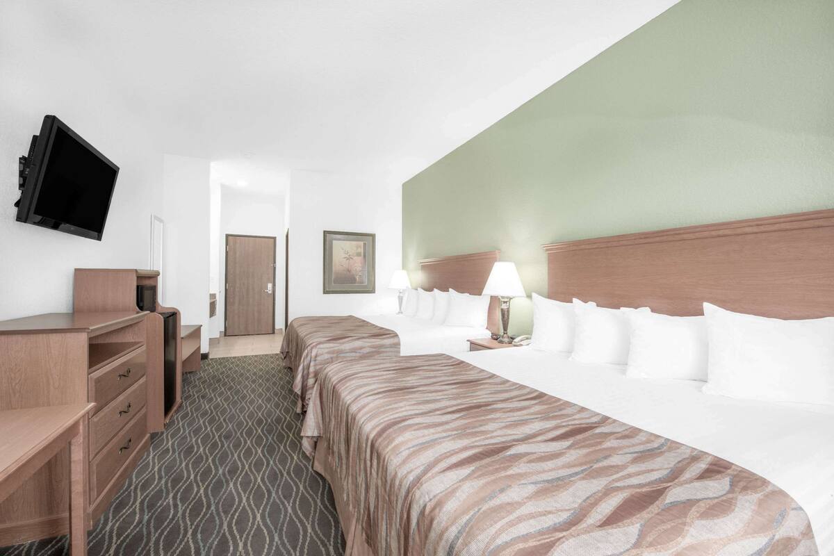 A hotel room with a bed, bedside tables, a desk, a TV, and a door.