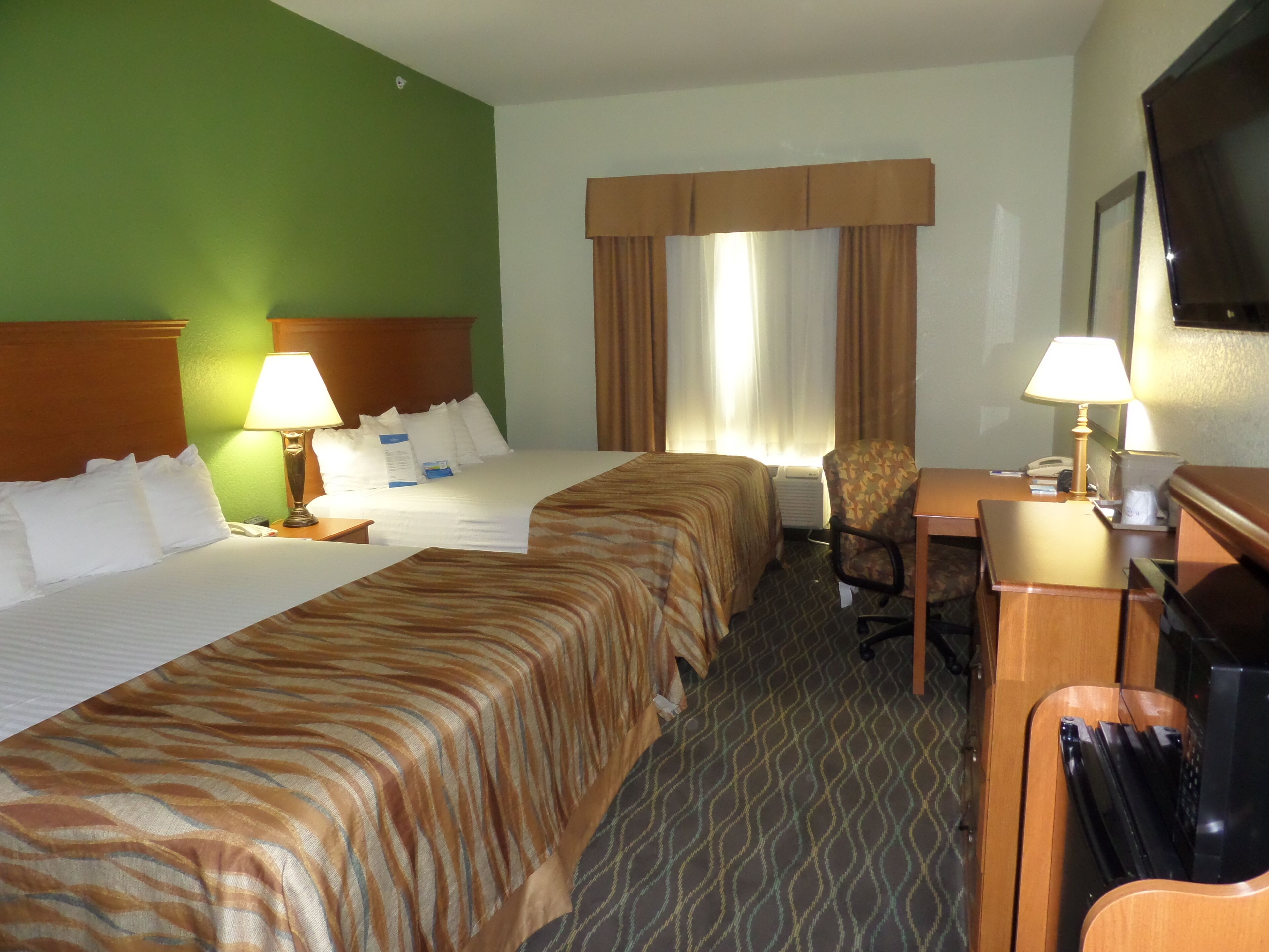 A hotel room with two beds, a desk, a chair, a television, and a window with curtains.