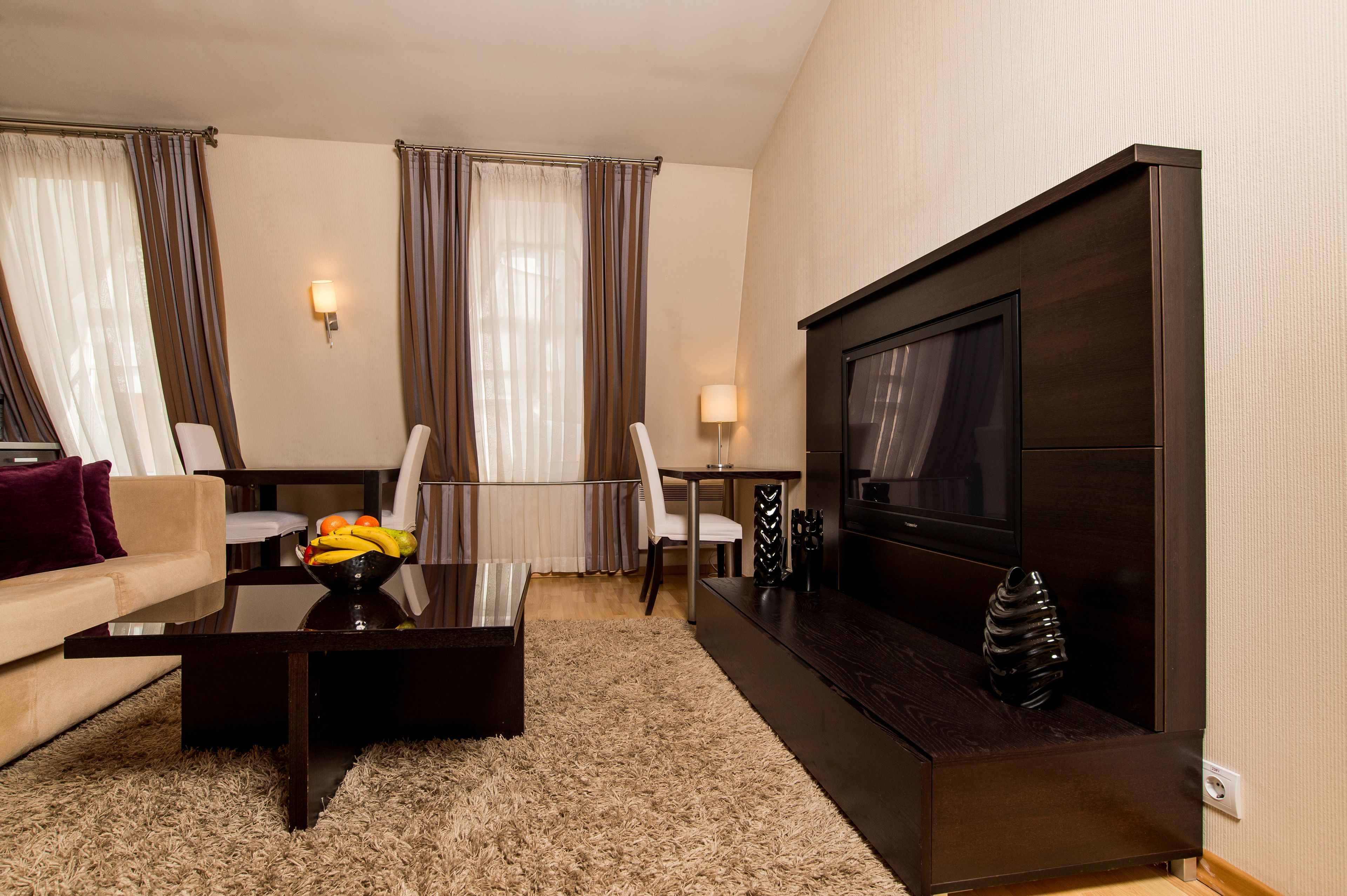 A modern living room with a sofa, coffee table, TV, and a dining area with chairs and a table.
