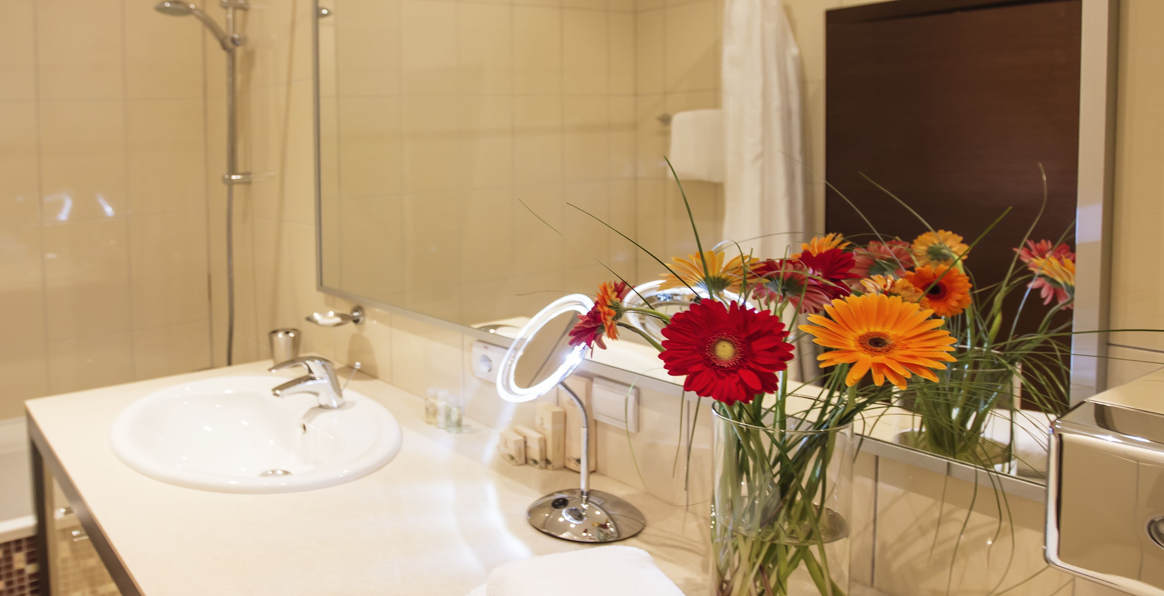 Un baño con un lavamanos blanco, un espejo y un jarrón con flores.
