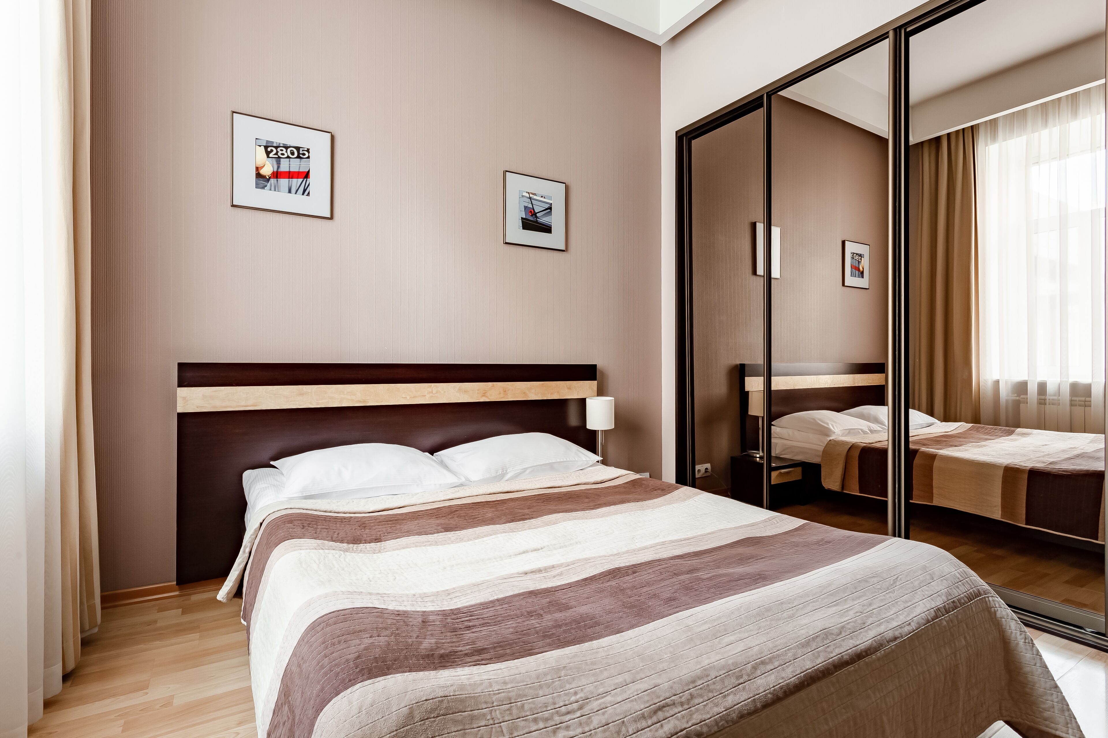 A hotel room with a large bed, a bedside table, a mirror, and two framed pictures on the wall.