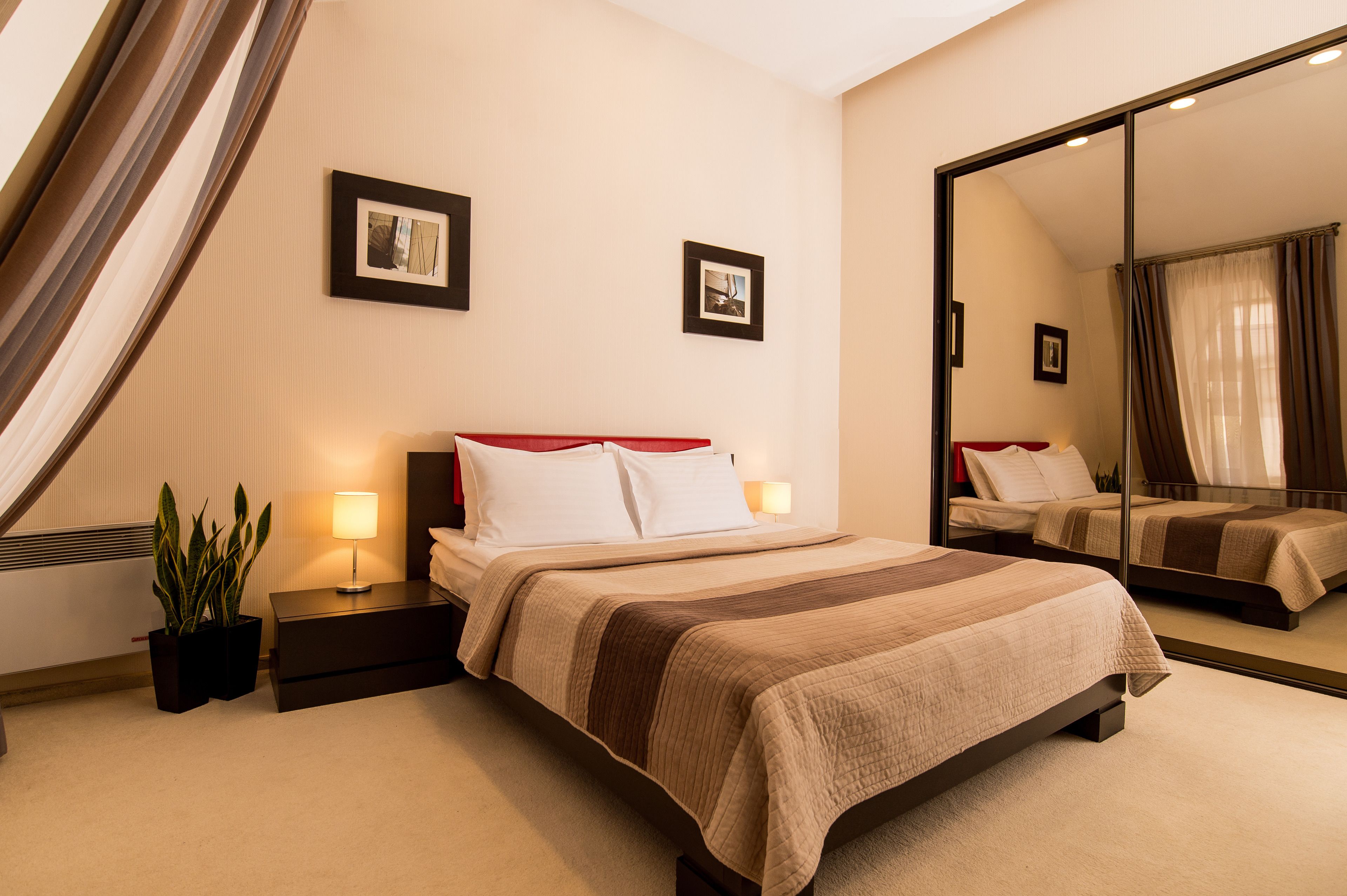 Une chambre d’hôtel avec un grand lit, des tables de chevet, un miroir et deux tableaux encadrés au mur.