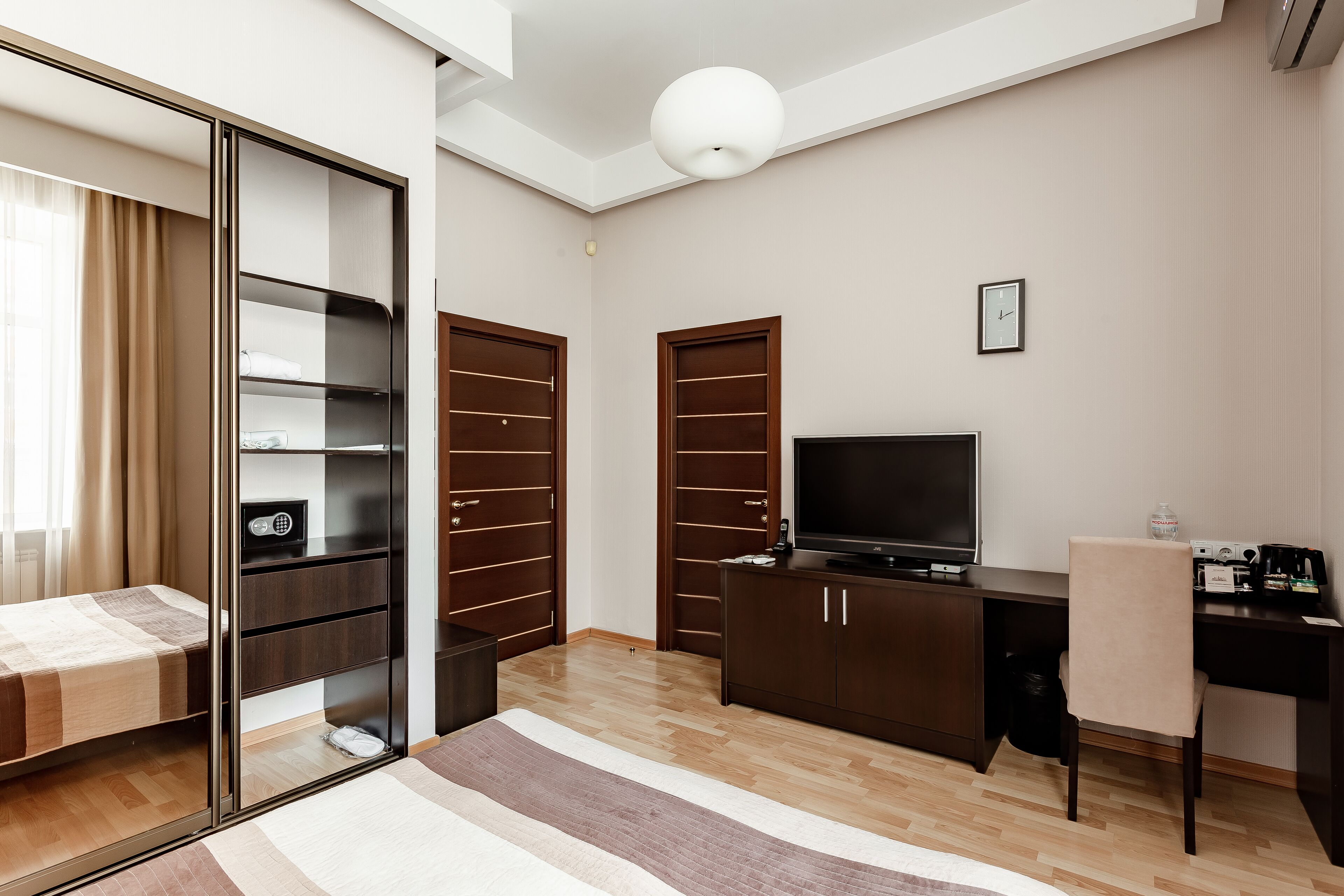 A modern hotel room with a bed, a desk, a TV, and a wardrobe.
