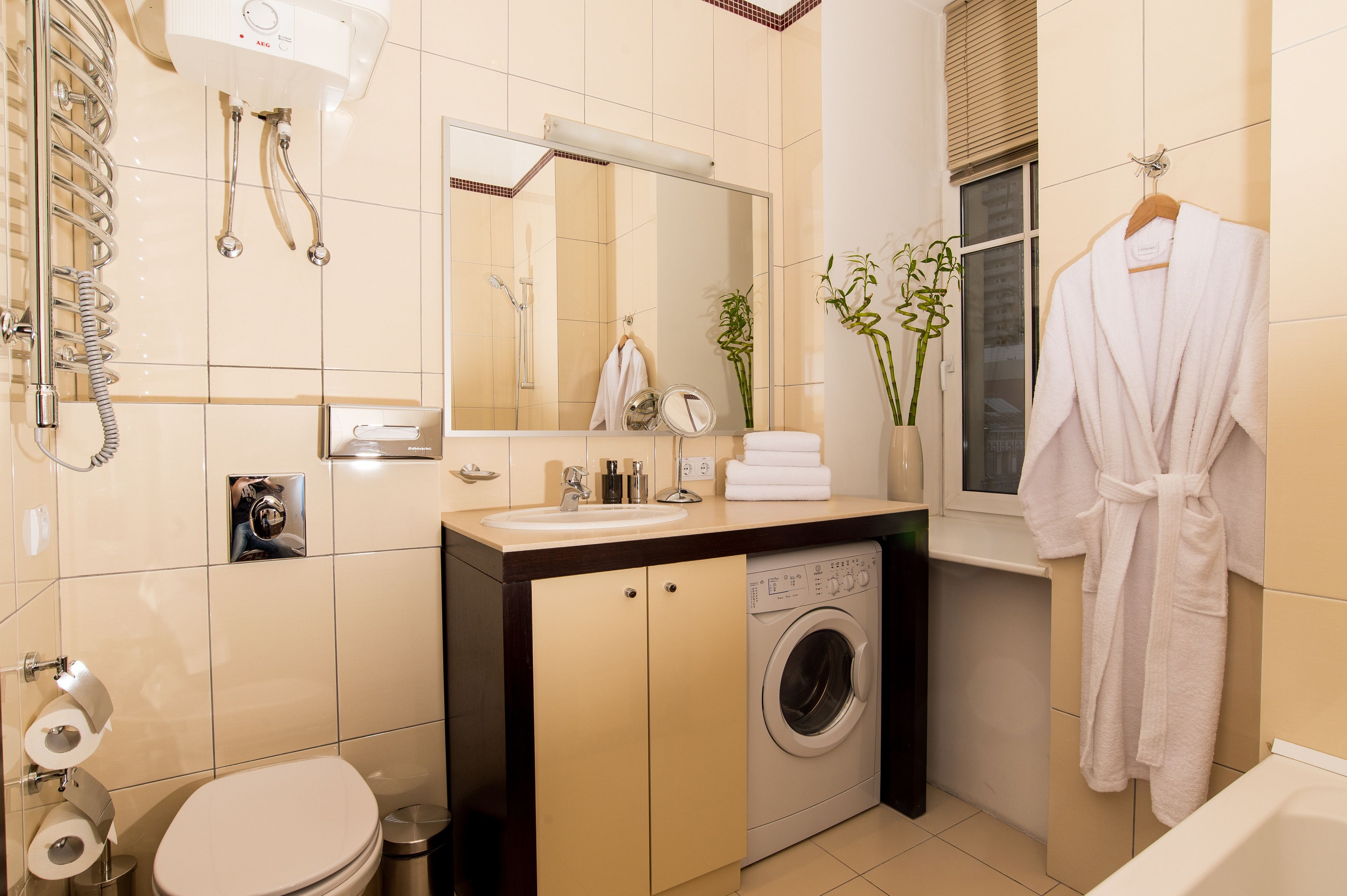 A modern bathroom with a built-in washing machine, a large mirror, and a towel rack.