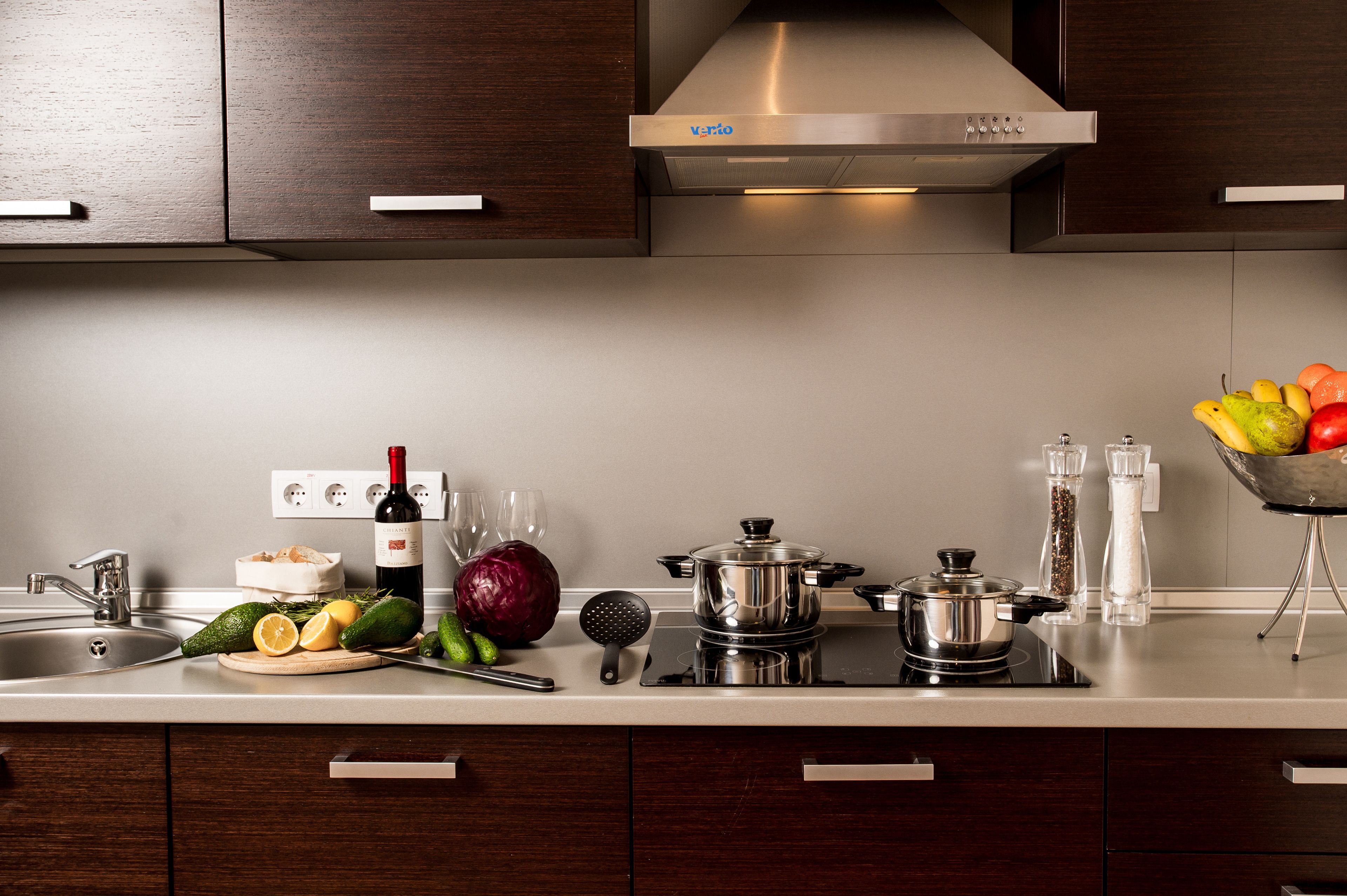 Una cocina moderna con electrodomésticos de acero inoxidable, una botella de vino, verduras frescas y un bol de fruta.