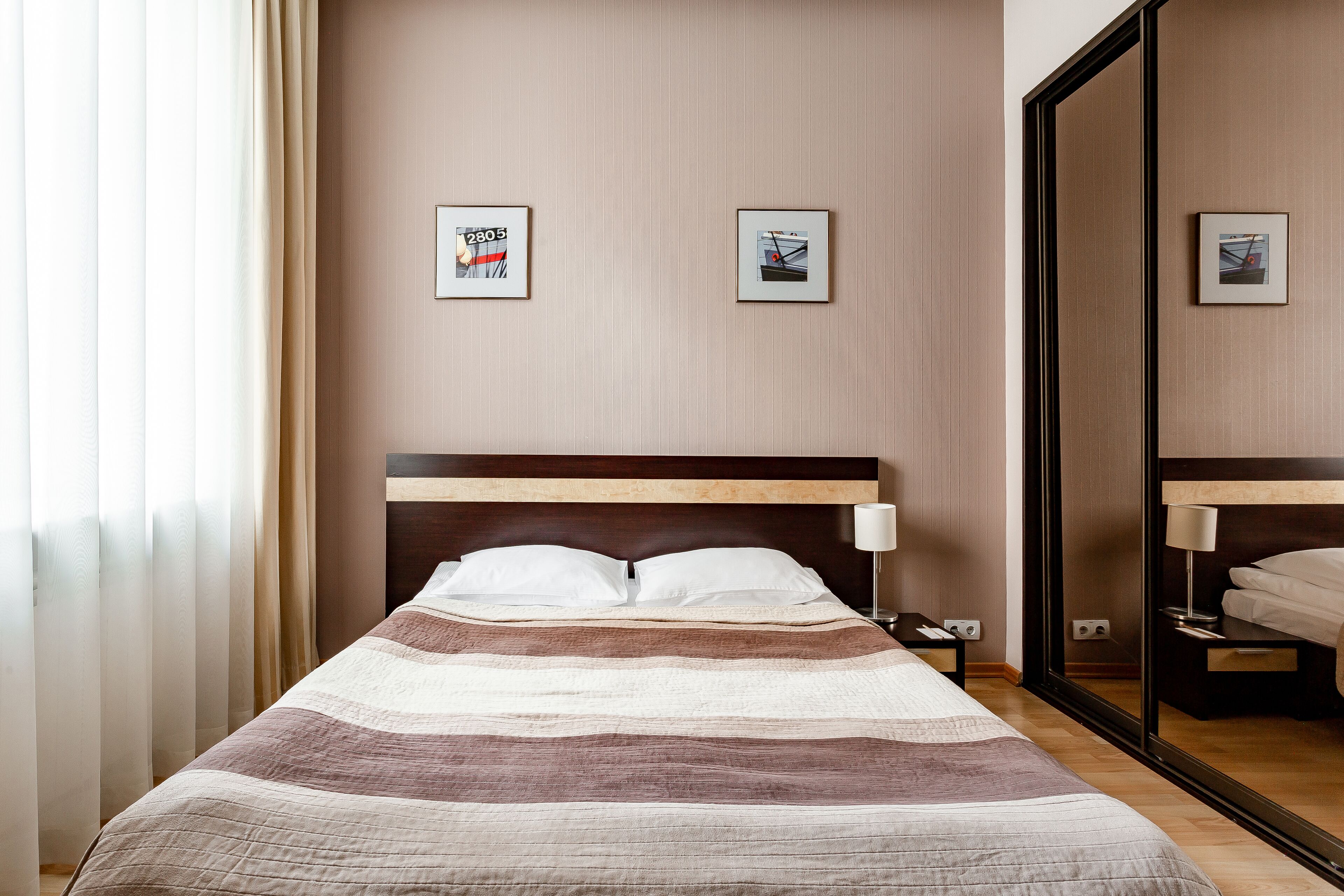 A hotel room with a bed, a nightstand, a mirror, and two framed pictures on the wall.