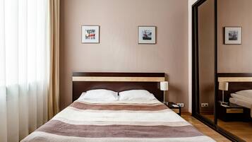 A hotel room with a bed, a nightstand, a mirror, and two framed pictures on the wall.