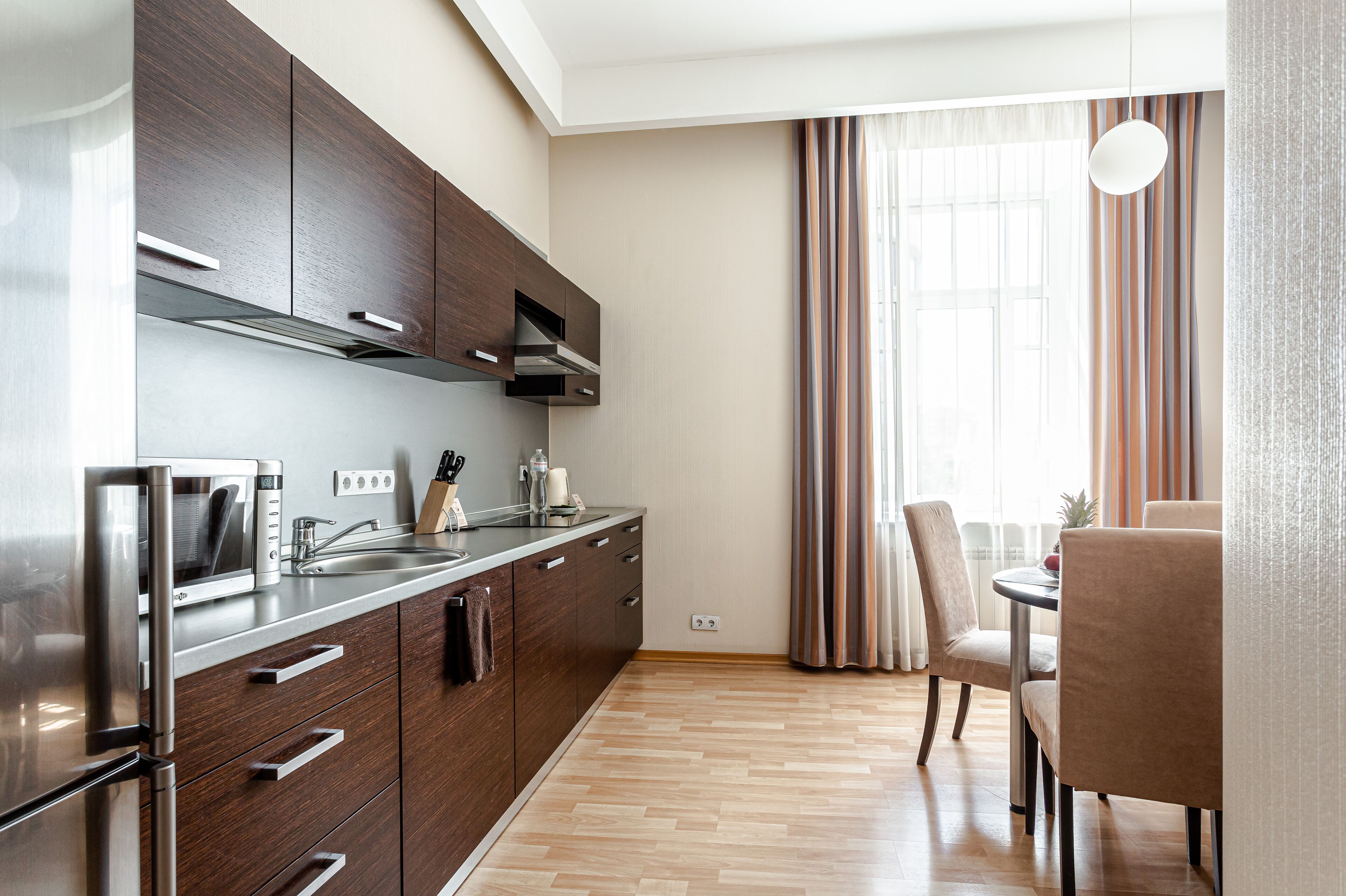 A modern kitchen with stainless steel appliances, wooden cabinets, and a dining area with a table and chairs.