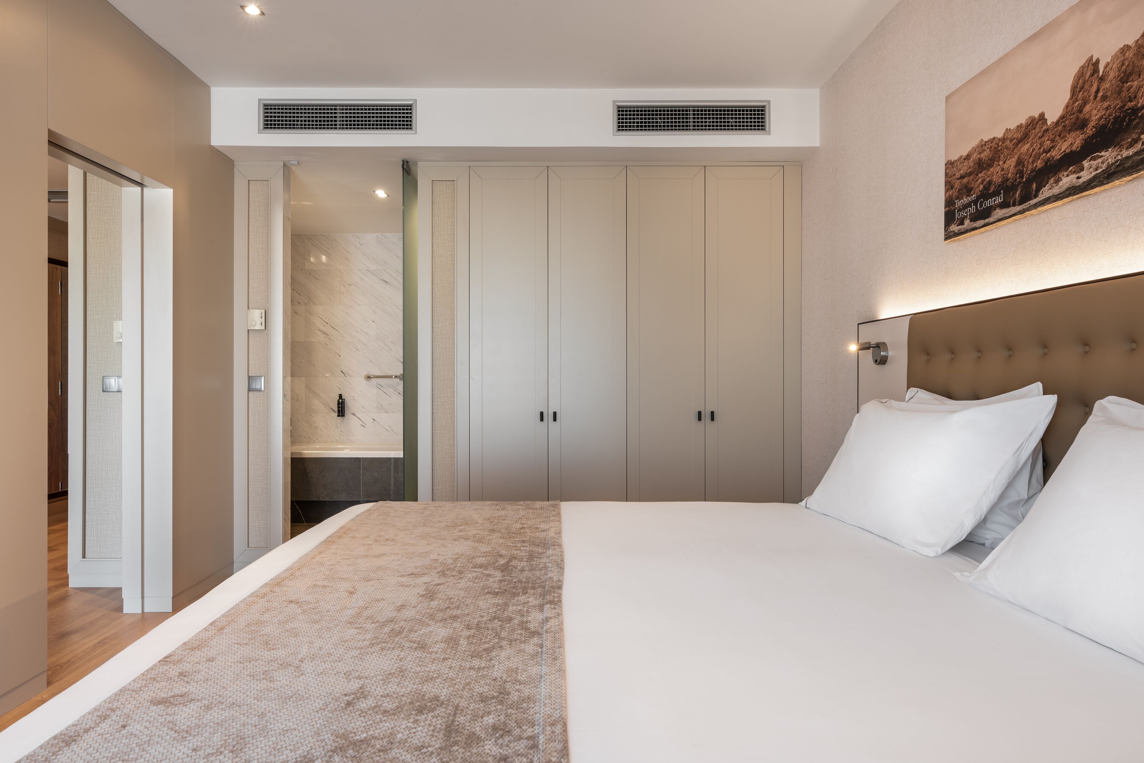 Un dormitorio moderno con una cama grande, un vestidor y un baño con pared de mármol.