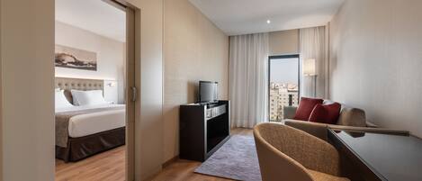 Habitación de hotel con cama, escritorio con silla, televisor y vista a la ciudad a través de una ventana.