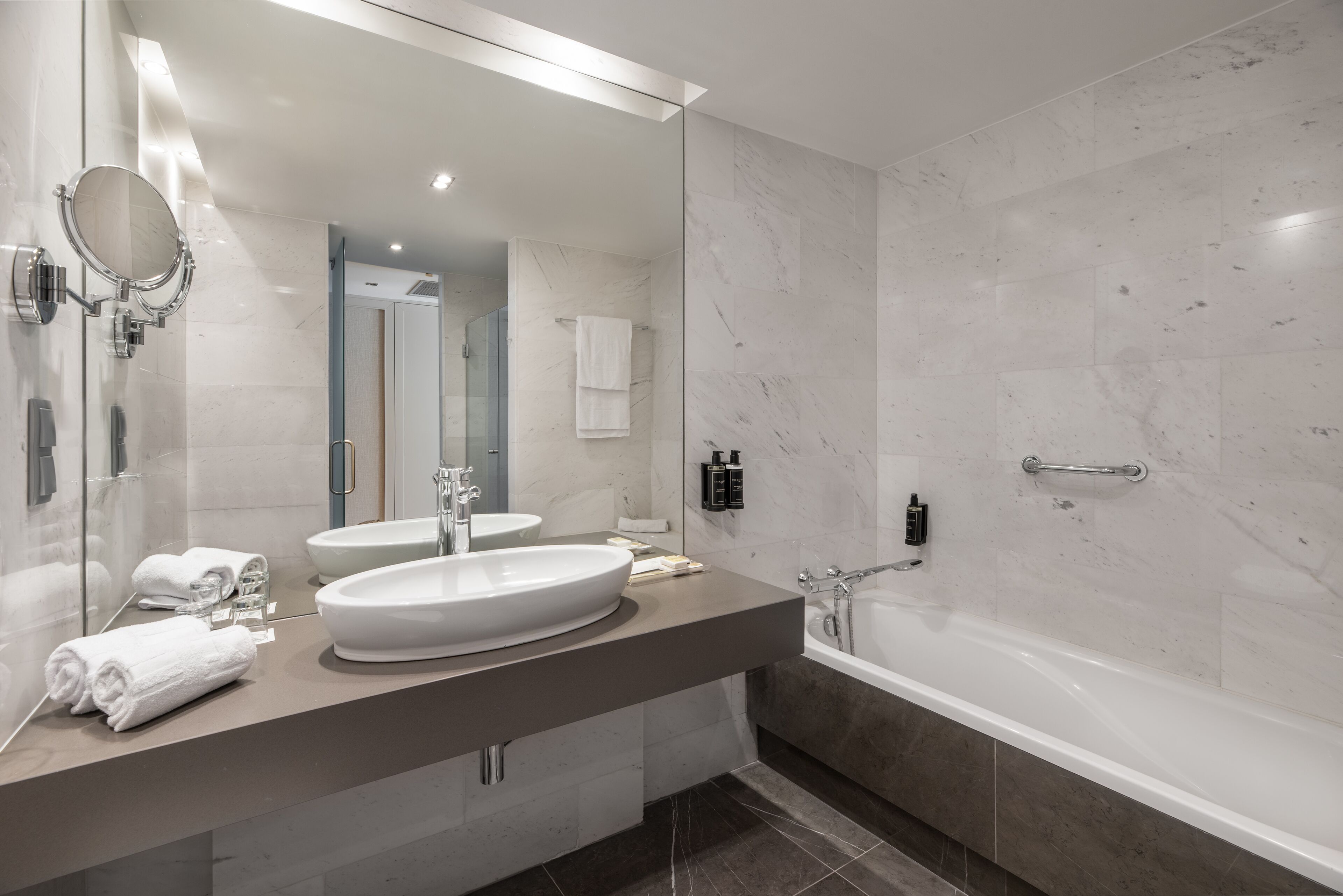 Un baño moderno con un espejo grande, dos lavamanos, una bañera y una cabina de ducha de vidrio.