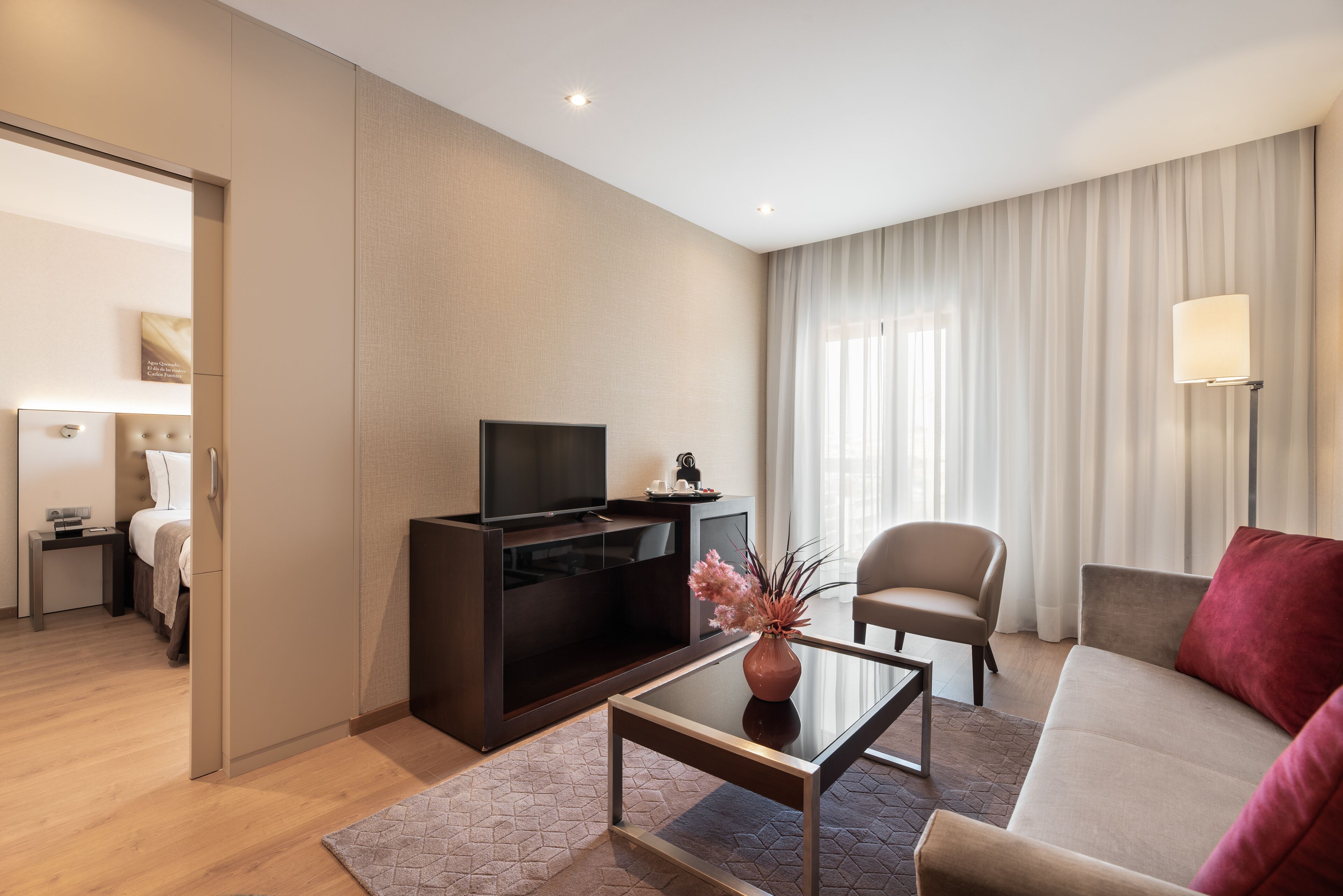 A modern hotel room with a flat-screen TV, a sofa, a coffee table, and a bed.