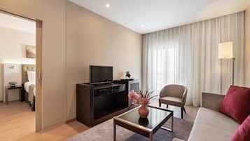 A modern hotel room with a flat-screen TV, a sofa, a coffee table, and a bed.