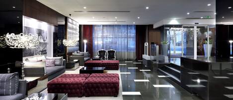A modern hotel lobby with a seating area, a reception desk, and a staircase leading to the upper floors.