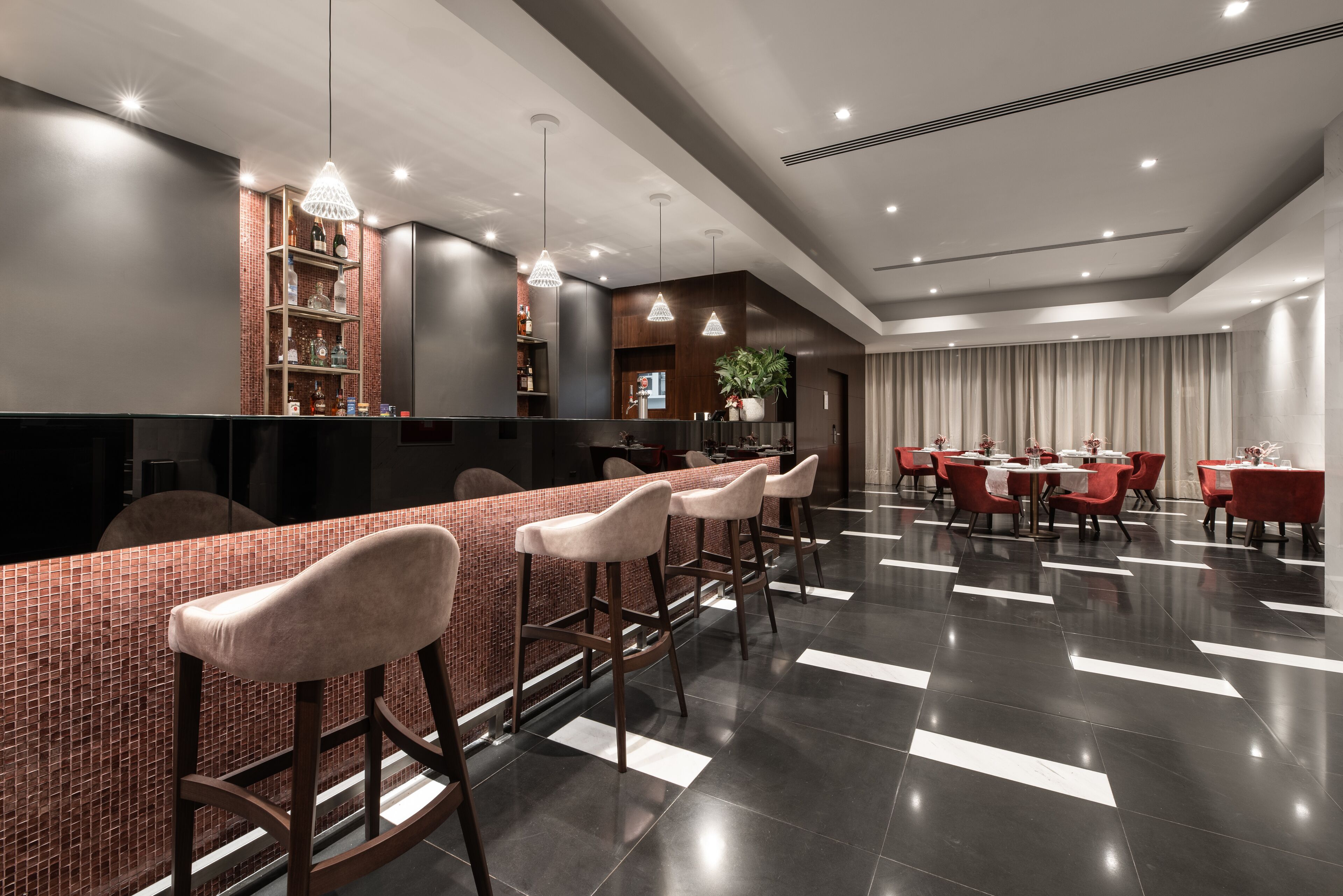 Eine moderne Bar mit einer langen Theke, mehreren Barhocker und einer Sitzecke mit Tischen und Stühlen.