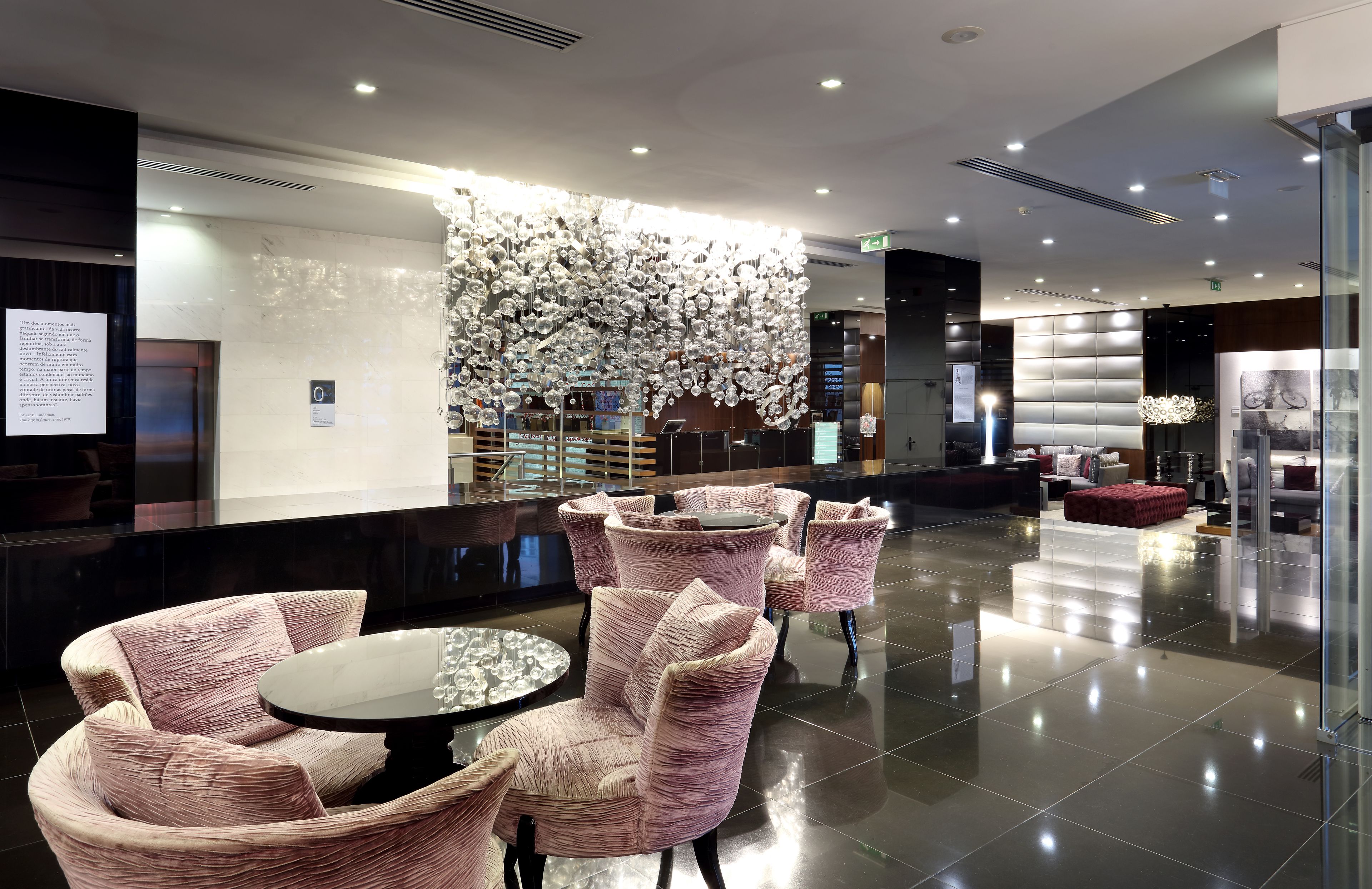 A modern lobby with a reception desk, seating area with round tables and chairs, and a decorative light installation.