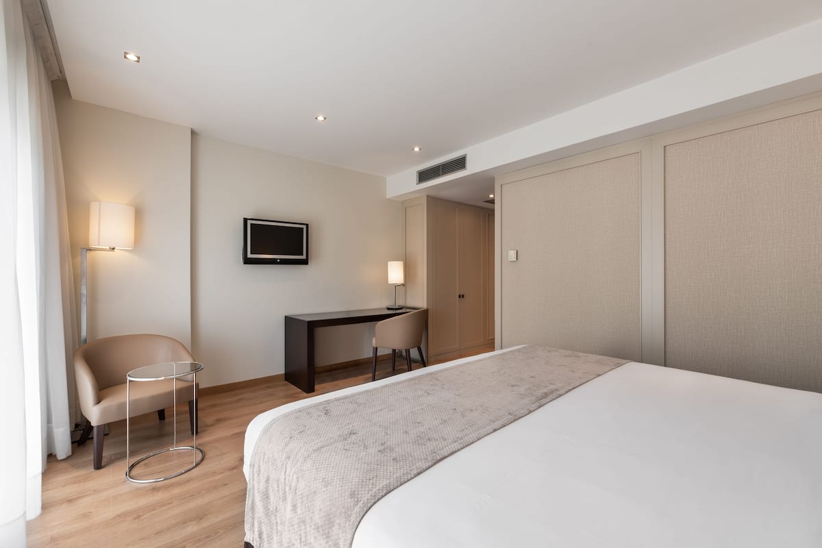 A modern hotel room with a large bed, a desk, a chair, and a television.