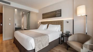 Una habitación de hotel moderna con una cama grande, una mesita de noche, una silla y una lámpara fijada a la pared.