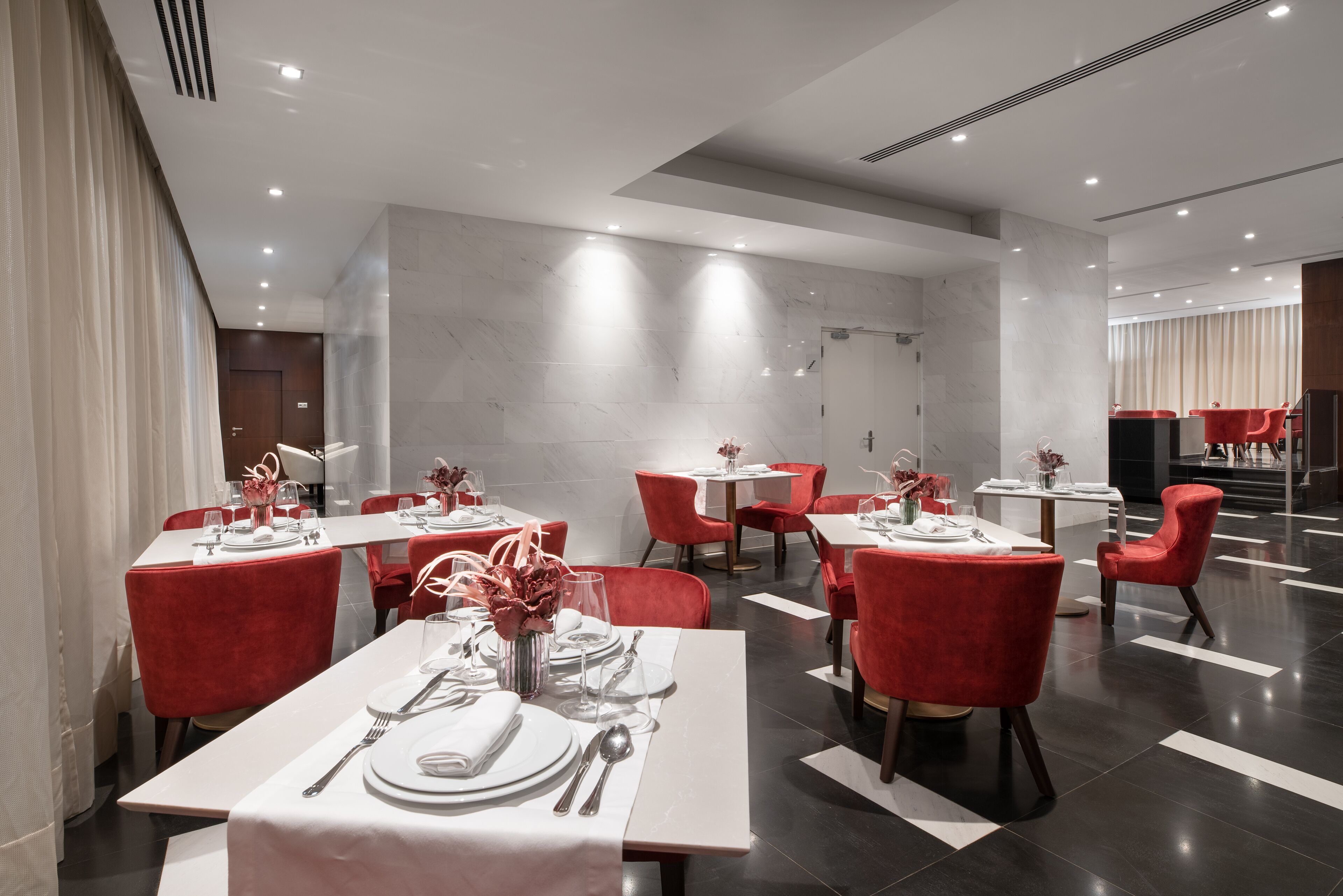 Un comedor moderno con mesas blancas, sillas rojas y una pared de mármol.
