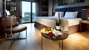 Habitación de hotel con cama, una mesa de comedor con una botella de champán, un plato de fruta y una rosa.