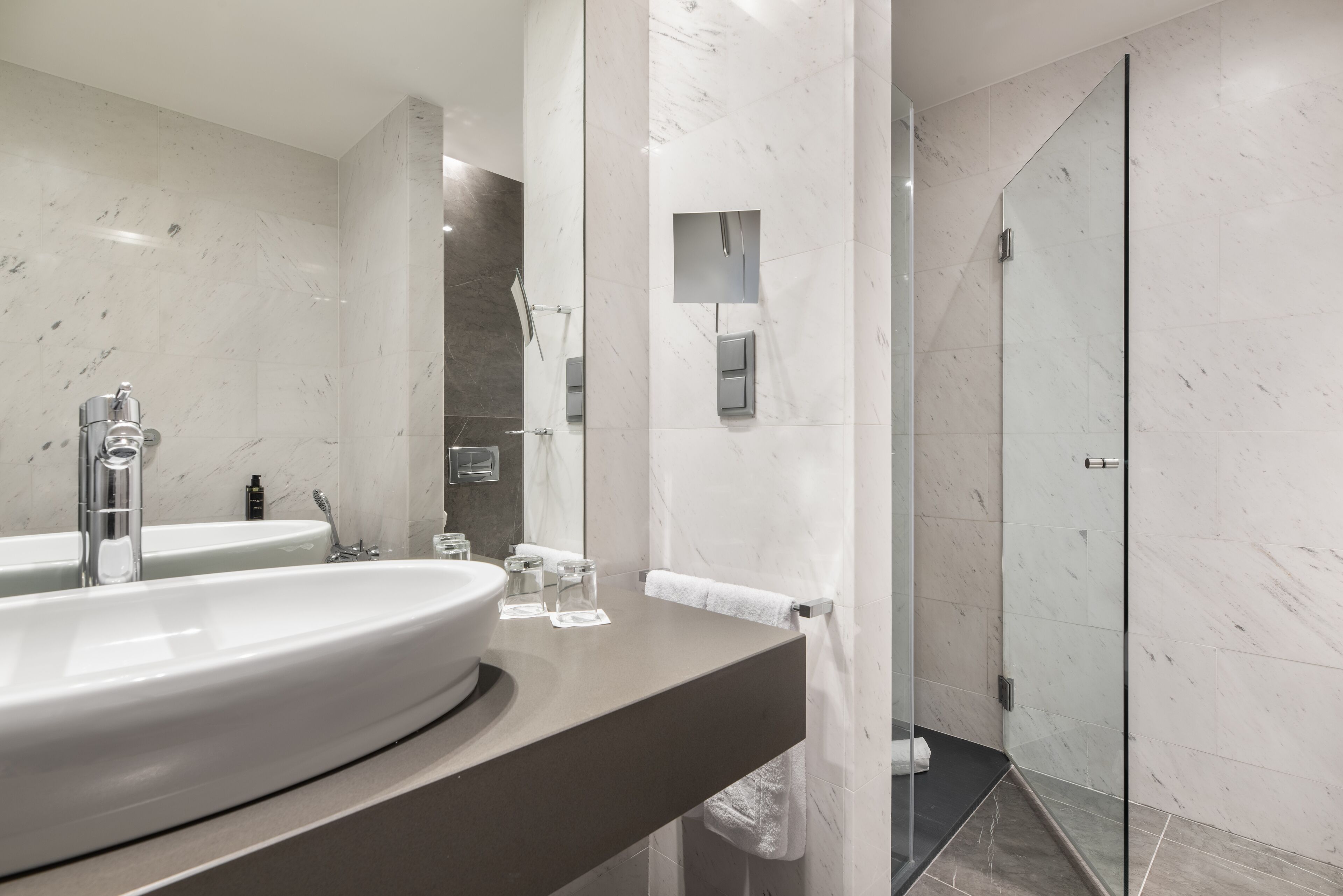 Un baño moderno con un lavamanos grande, una cabina de ducha con mampara de vidrio y paredes de mármol.