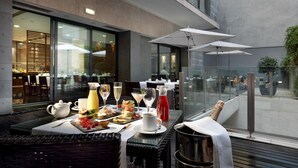 Una mesa de comedor dispuesta con comida, bebidas y una botella de champán en una terraza al aire libre con vistas a la ciudad.