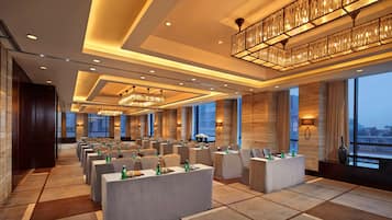 A spacious conference room with multiple tables and chairs, large windows, and modern lighting fixtures.